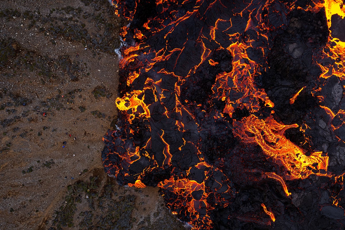 Aerial view of yellow-red and black lava flow showing the line where the lava is has not yet reached on the left.