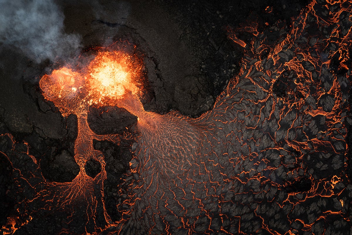 Aerial view of erupting volcano showing the source crater and lava flowing out.