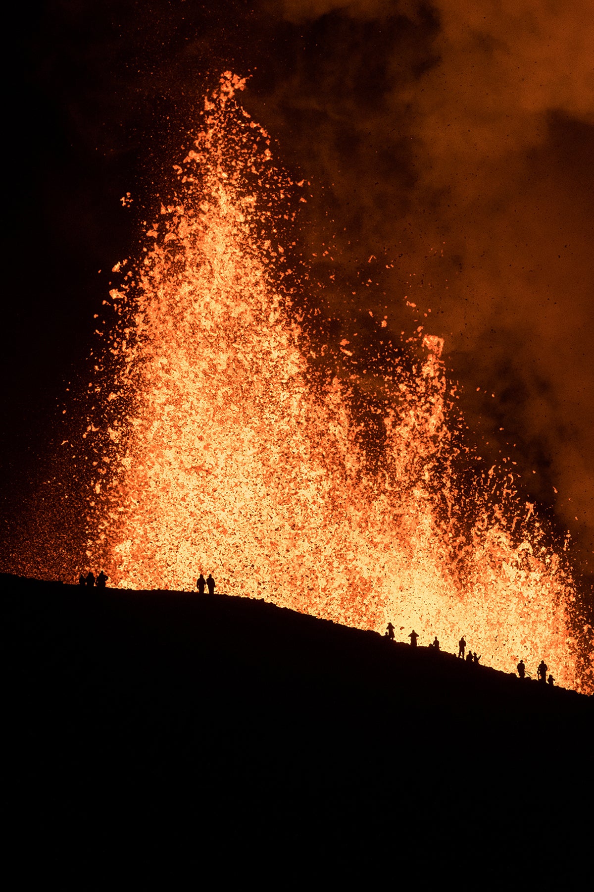 Landscape showing small human figures in silhouette, with lava exploding in the background.