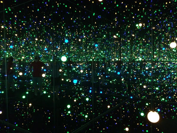 A dark mirrored room with green, blue, and yellow lights and their reflections