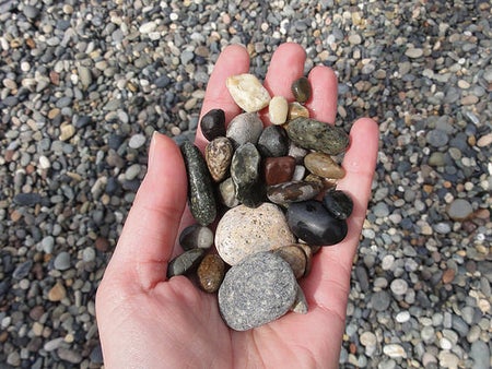 Image shows a hand holding a palm full of beach pebbles.
