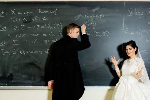 Nikita Nikolaev writes mathematics on a blackboard while Beatriz Navarro Lameda watches. He is wearing a tuxedo, and she is wearing a white wedding gown.