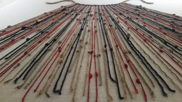 Many off-white, black, and red knotted cords attached to a cord at the top