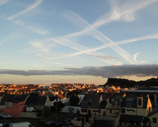 A blue sky with streaks of clouds forming a tic-tac-toe pattern over the tops of some houses