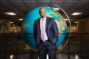 J. Marshall Shepherd in a suit, standing in front of a large world globe.