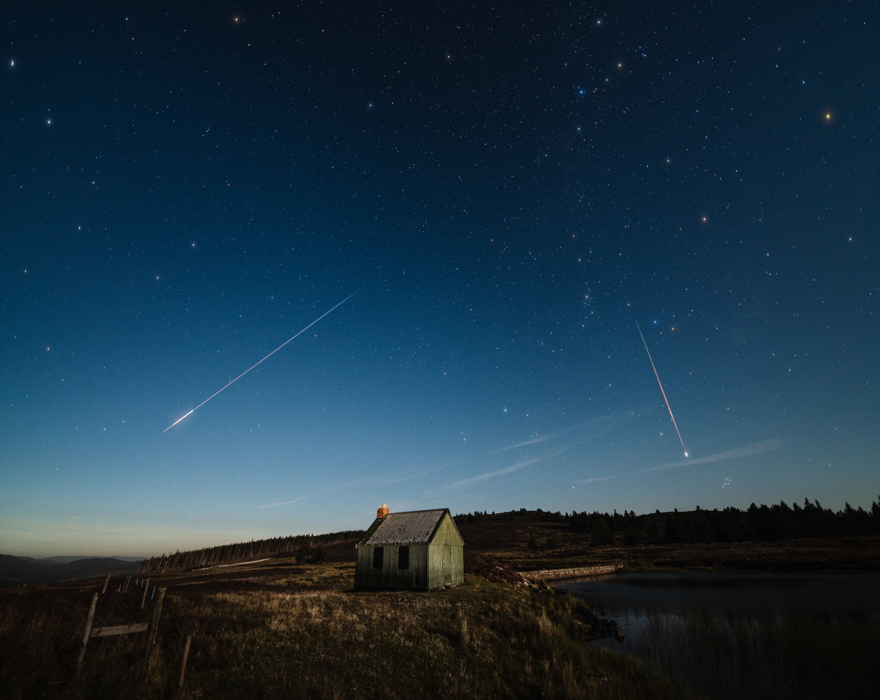 Several meteors streak across the night sky over a small house in the countryside