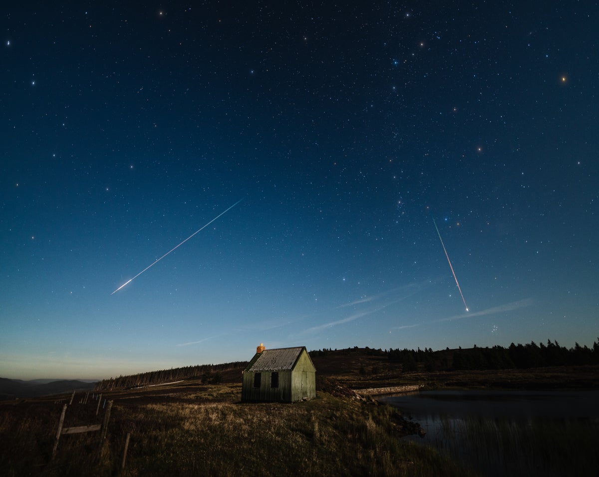 Several meteors streak across the night sky over a small house in the countryside