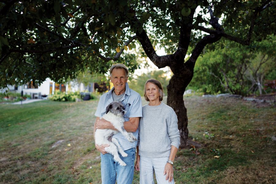 A man and woman stand holding a small dog in front of a gnarled 300-year-old apple tree.