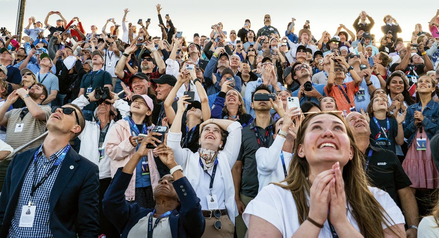 A crowd of emotional observers looks up and reacts to the Artemis II rocket as it soars into the sky.
