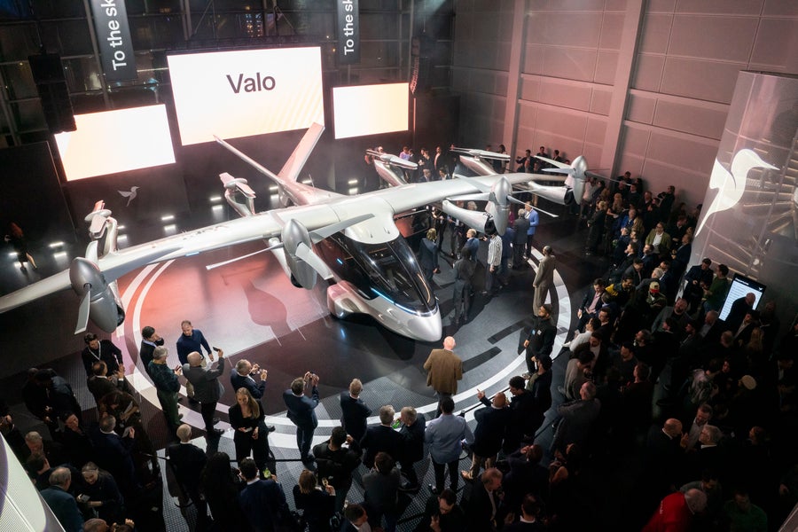 Vertical’s Valo electric aircraft is displayed on a circular stage at a crowded launch event, with large screens behind it reading Valo.