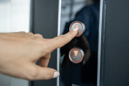Hand with manicure push the up button in elevator.