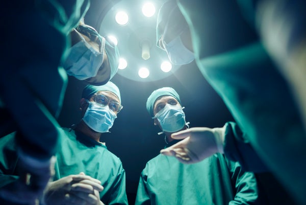 Upward-view of four surgeons leaning over patient from above