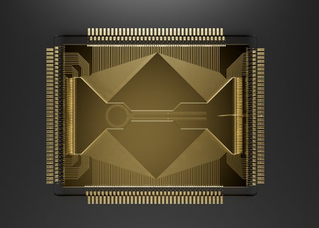 A gold square with etch marks along the edges and shapes on the top. The close-up photo shows a quantum processing chip.