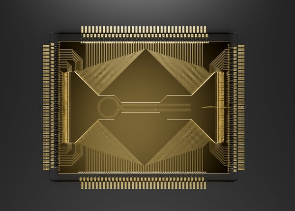 A gold square with etch marks along the edges and shapes on the top. The close-up photo shows a quantum processing chip.