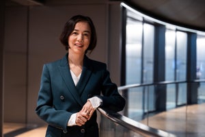 Fei-Fei Li leaning against a railing, smiling in a suit.