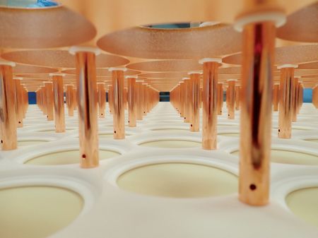 Rows of copper tubes rise from a white panel punctuated with an array of circular indentations inside the XENONnT dark matter detector. Provided by XENON Collaboration.
