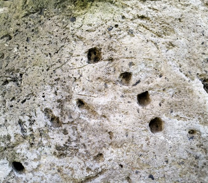 A close up of light gray stone showing a series of four holes moving downward from the top center in an arc