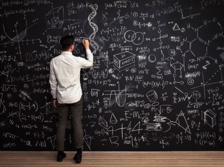 Man writes mathematical equations on chalkboard.