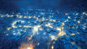 Overhead view of several houses with roofs covered in snow clustered around well-lit streets at night.