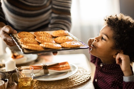 A small child at a table smells a platter of baked goods.