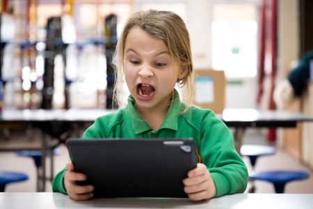 Kid looks at a tablet in shock