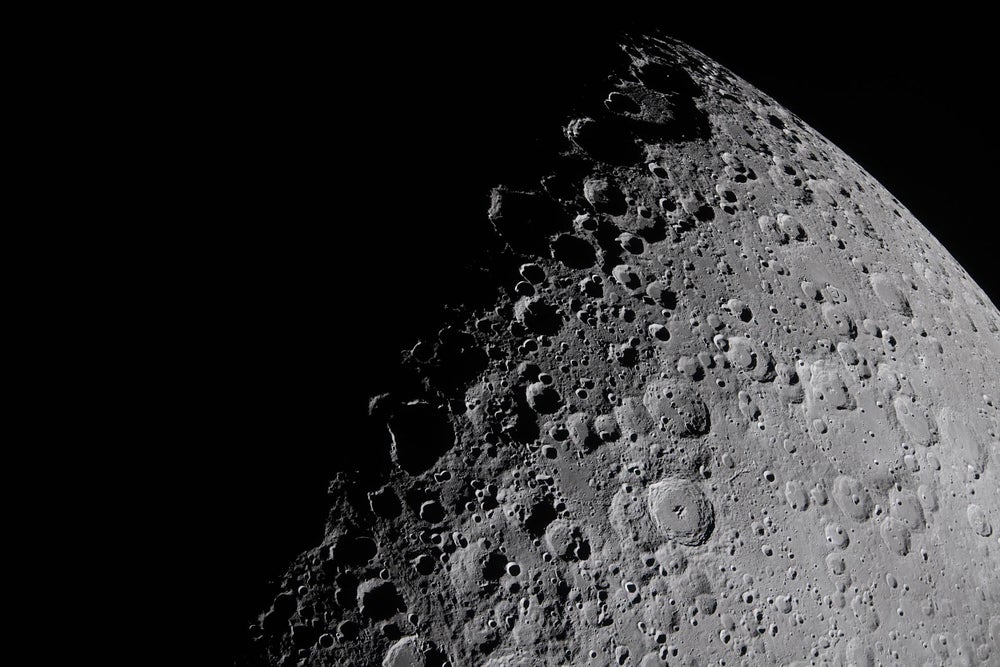 Primer plano de una luna cubierta de cráteres con la mitad oscurecida por la oscuridad, el borde cruza de abajo a la izquierda hacia arriba a la derecha.
