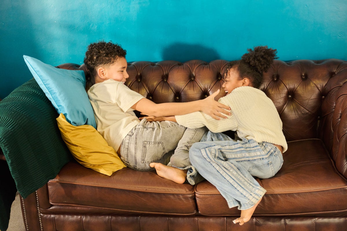Two children playfully pushing and laughing together on a sofa in a bright home interior