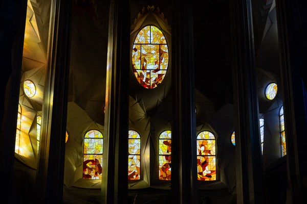 Light pours through tall, geometric stained-glass windows inside a dark church interior.