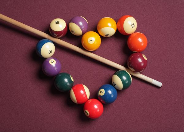 A number of billiard balls assembled in the shape of a heard with a pool cue cutting through the middle