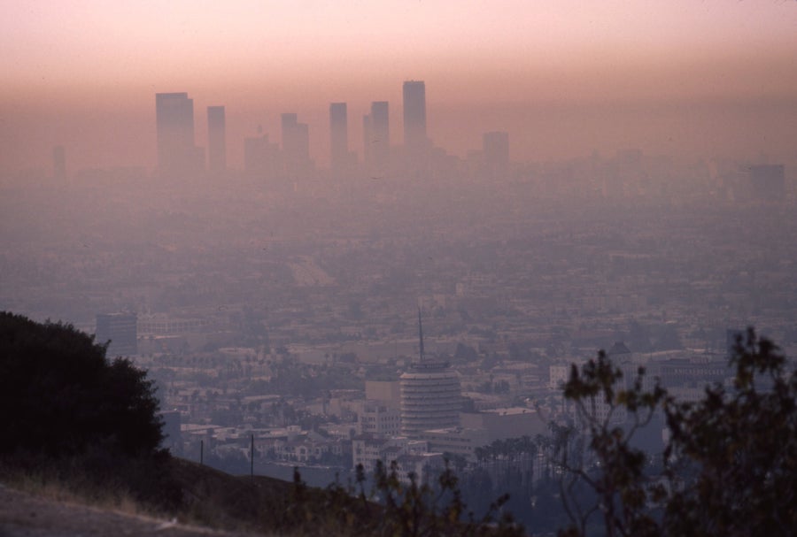 A pinkish brown haze obscures the Los Angeles city skyline with the Capitol Records building in the foreground seen from Mulholland Drive