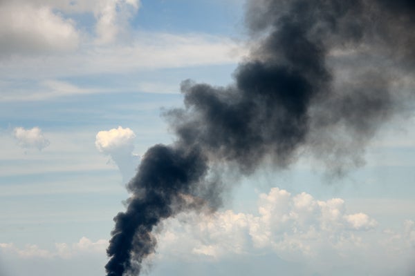 Blue sky with a trail of black smoke rising up