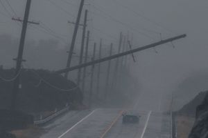 A power pole leans over a highway with a single car in rainy conditions.