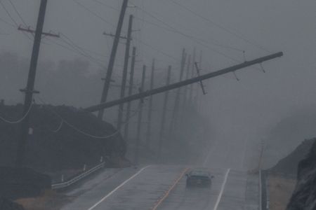 A power pole leans over a highway with a single car in rainy conditions.