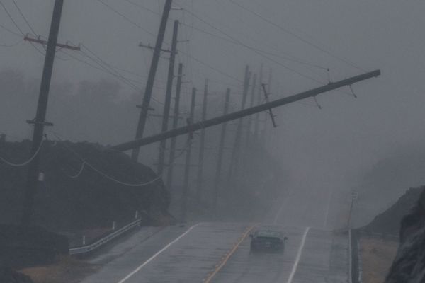 A power pole leans over a highway with a single car in rainy conditions.
