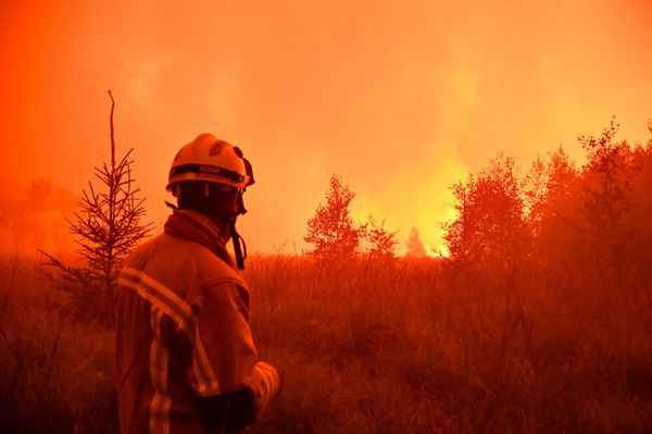 A firefighter looks toward a glowing fire.