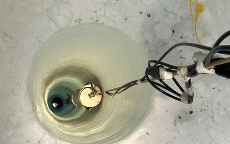 A close up of a drill drilling into a thick chunk of ice.