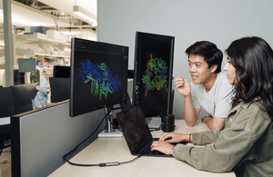 Brian Hie and Aditi Merchant examine a protein structure generated by Evo 2, an AI tool that can suggest genome designs. Lab tests of Evo 2’s designs for an E. coli killer exceeded expectations.