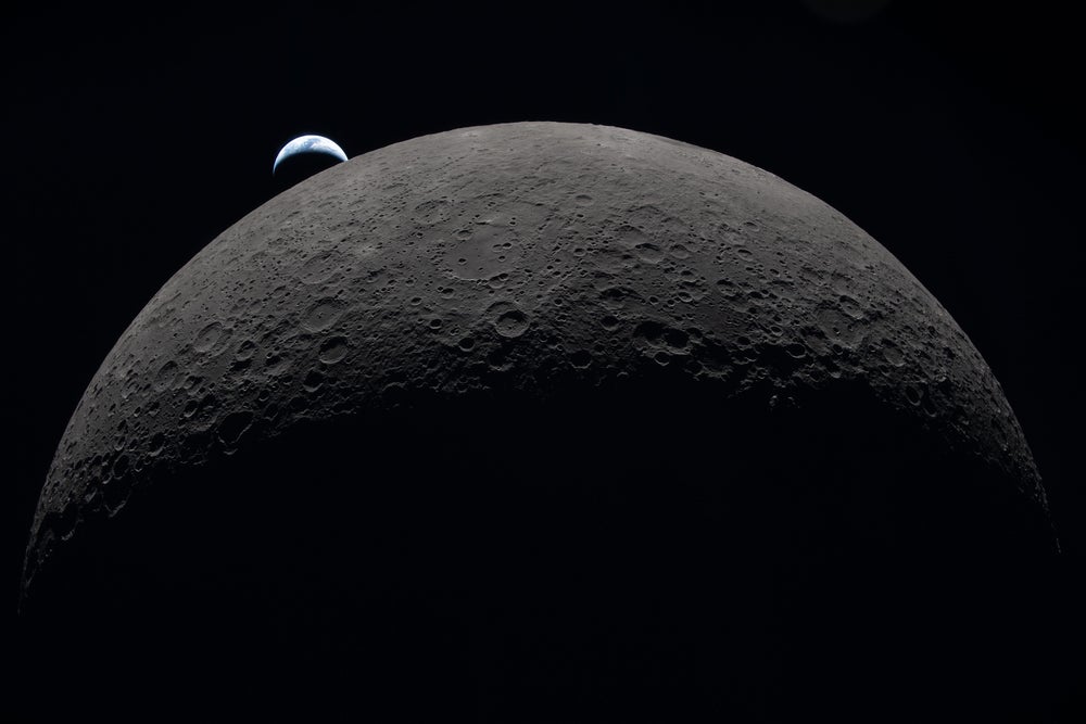 Una vista de la mitad del disco de la luna, coronado por una pequeña Tierra en cuarto creciente.