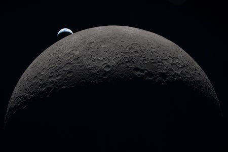 A view of half the moon's disk, topped by a tiny crescent Earth.