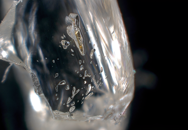 A close-up of a clear, polished diamond with small specks that look like bubbles but are small bits of minerals