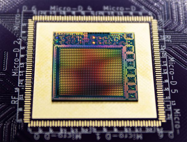 A chip with a rainbow reflection sits on a processor board.