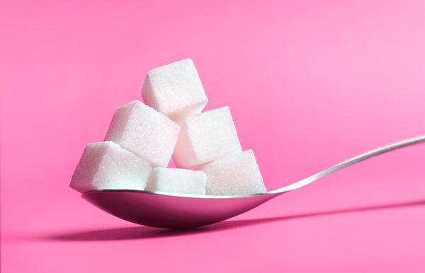 A spoonful of sugar cubes on pink background.