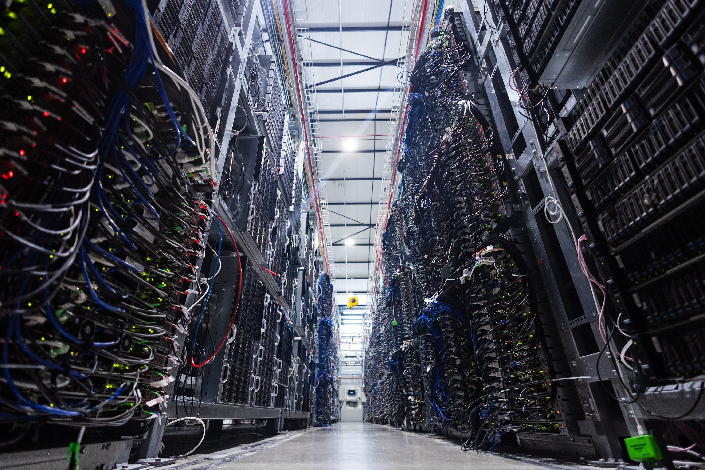 Rows of tall server racks filled with cables and blinking lights line a data center aisle.