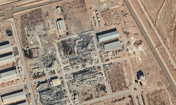 A satellite image looking directly down at an industrial complex in flat, brown landscape with visible damage to several buildings