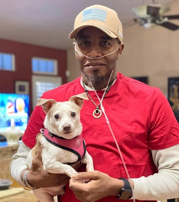 Bertrand Nelson weaing a red shirt and baseball cap and holding a small dog.