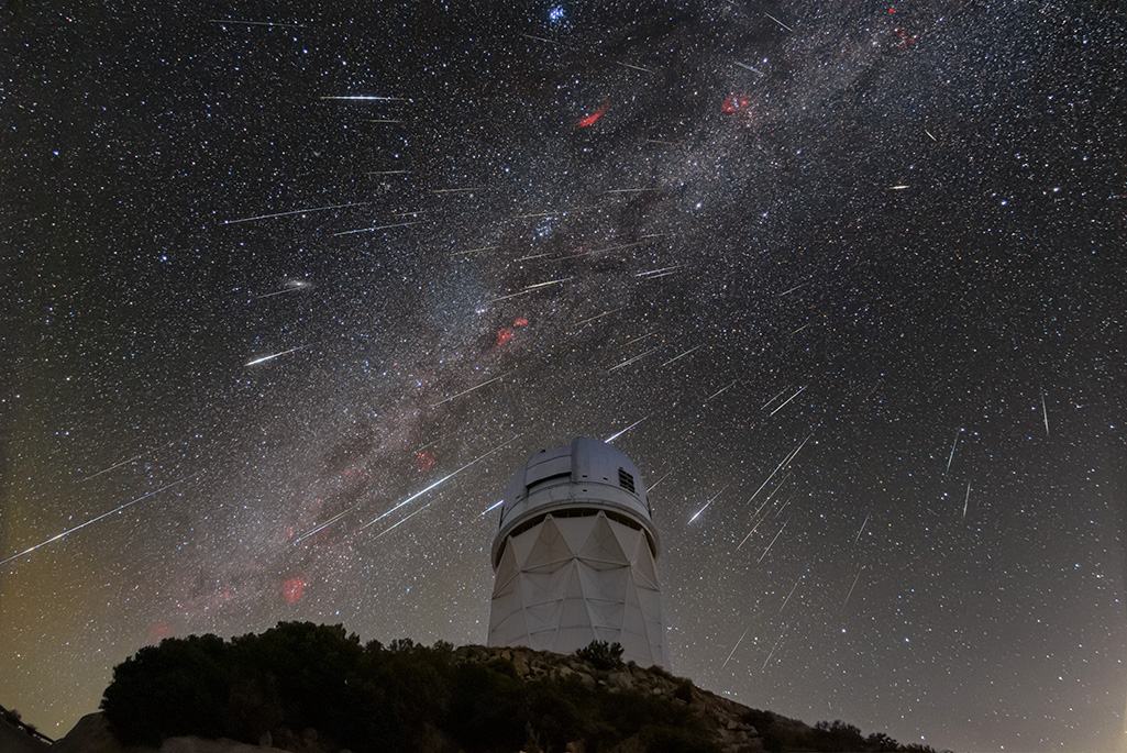 A telescope on a hilltop against a starlit night sky with meteors ablaze