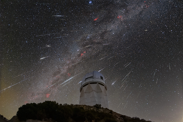 A telescope on a hilltop against a starlit night sky with meteors ablaze