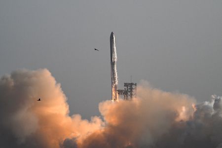 A rocket blasting off against a gray sky with a cloud of exhaust below it.