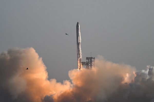 A rocket blasting off against a gray sky with a cloud of exhaust below it.