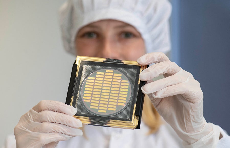 A woman wearing scrubs holds up a square quantum computer chip.